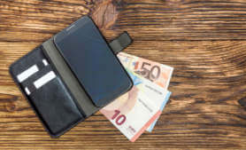Geldscheine liegen unter einem Smartphone.